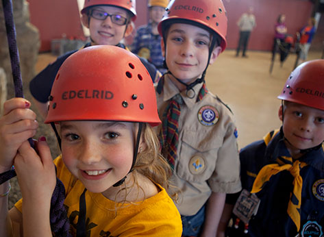 Group of smiling youth Scouts in climbing gear, ready to climb an indoor rock wall