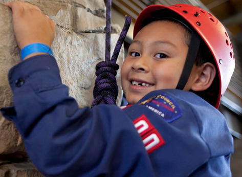 A happy Scout climbing an indoor rock wall