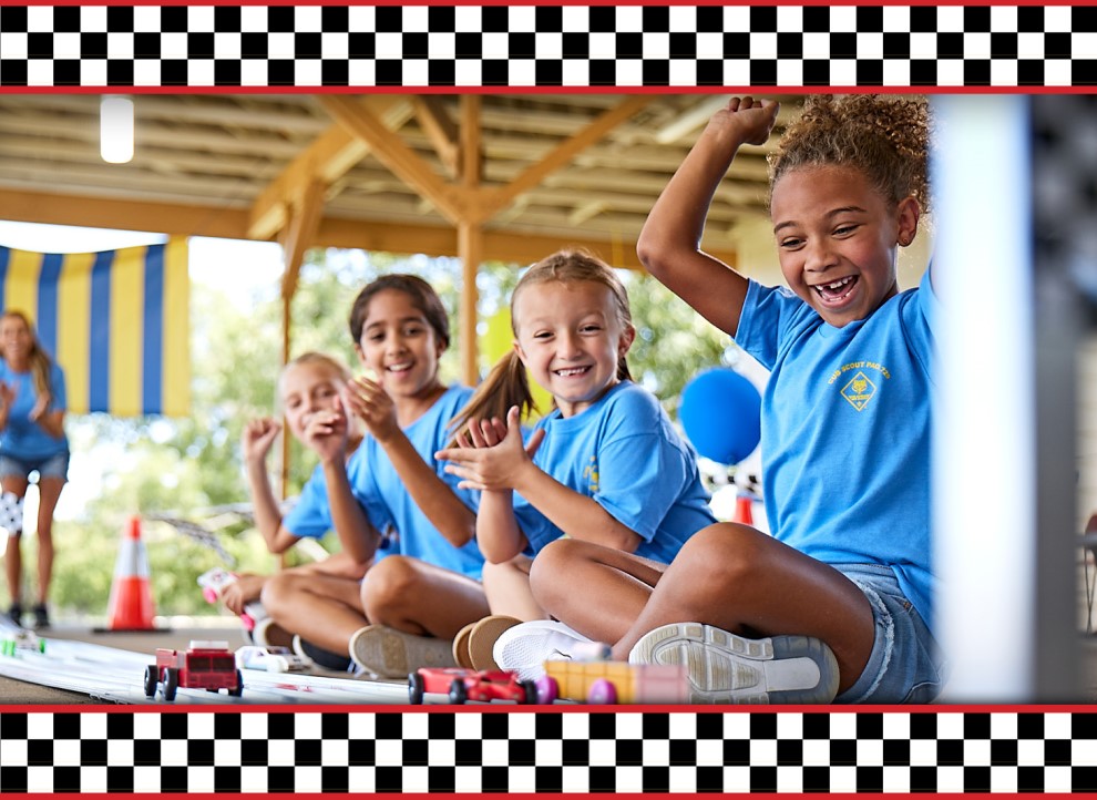 Group of female Scouts cheering as the end of a pinewood derby racetrack as cars near the finish