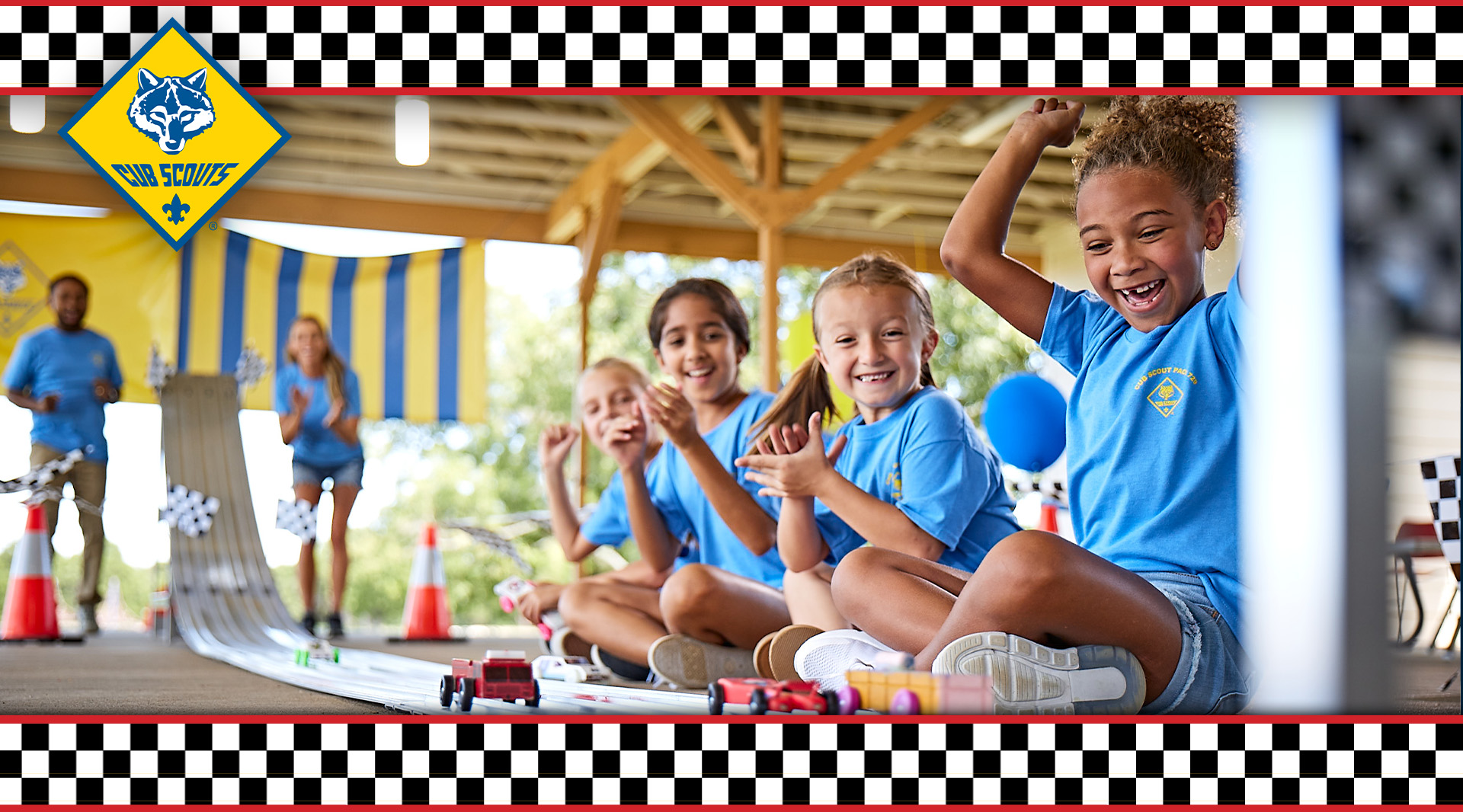 Group of female Scouts cheering as the end of a pinewood derby racetrack as cars near the finish